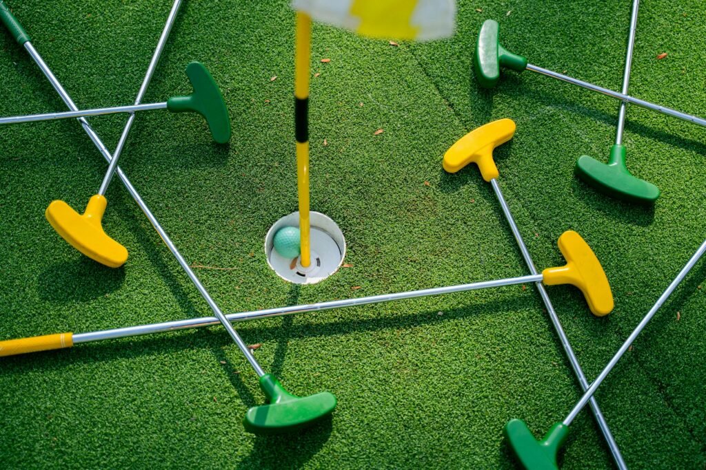 Top view of colorful mini golf putters around a hole on artificial grass.